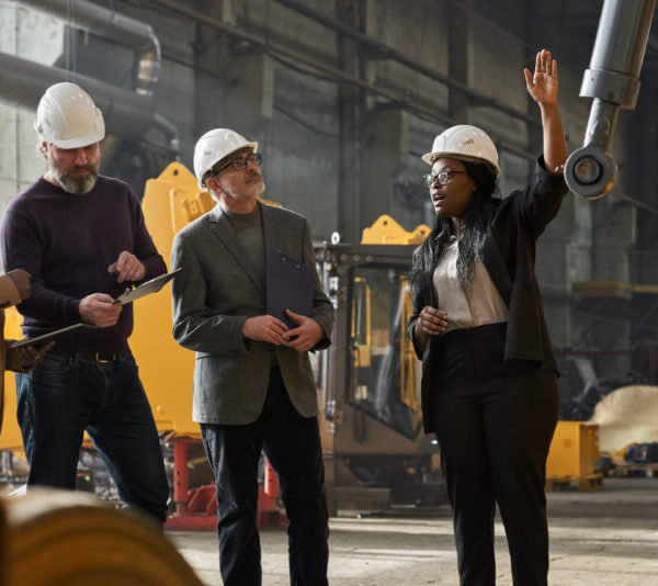 African businesswoman in work helmet presenting the new machine to business people at factory