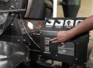 Close up of a man hand setting the buttons of a coffee roaster machine. Concept of local coffee production